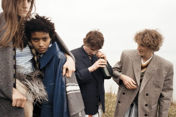 Veronica wears tracksuit top, top & feather-trimmed fur scarf by Prada. Manuela wears coat by Acne Studios, shirt by Prada, beach cap by Miu Miu. Roberts wears jacket by Balenciaga, shirt & sleeveless pullover by Prada, jacket around the waist by Stone Island, shorts by Acne Studios. Harold wears jacket by Balenciaga, sleeveless pullover & coat around the waist by Prada.